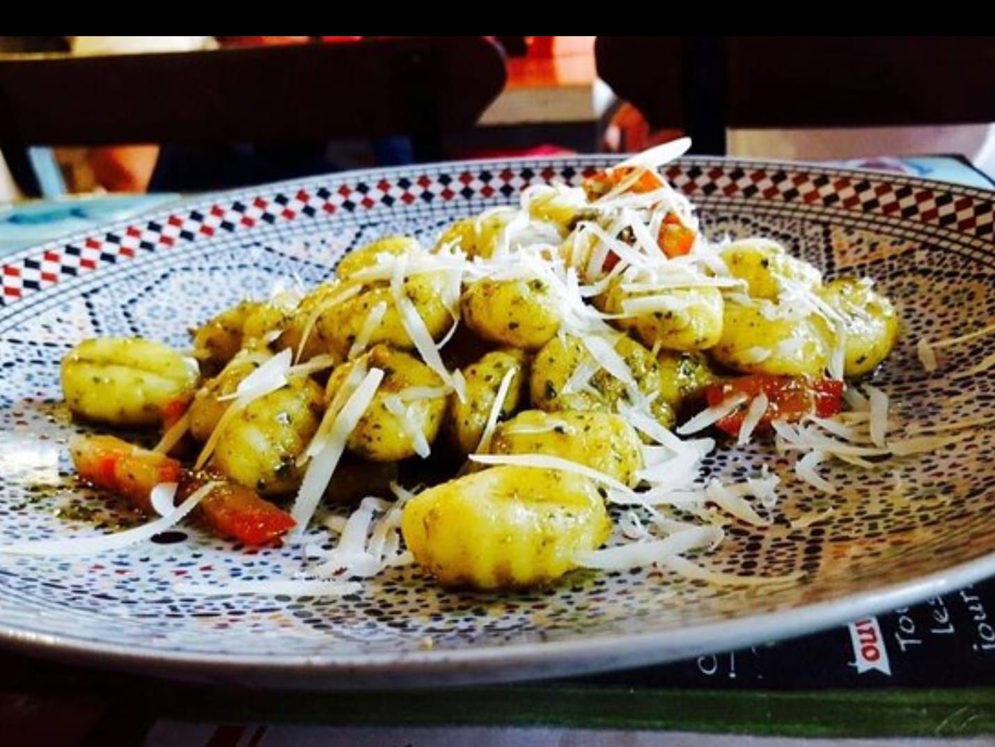Un plato de ñoquis con queso y tomates sobre una mesa.