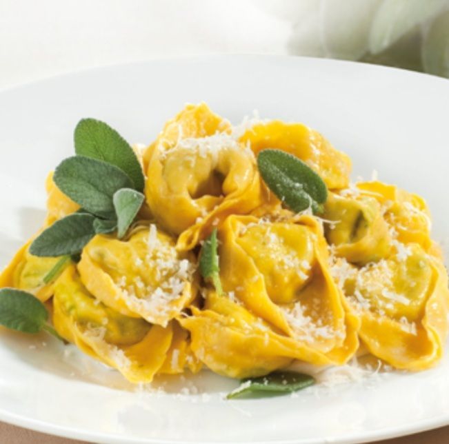 Un plato blanco cubierto con pasta amarilla y hojas verdes.