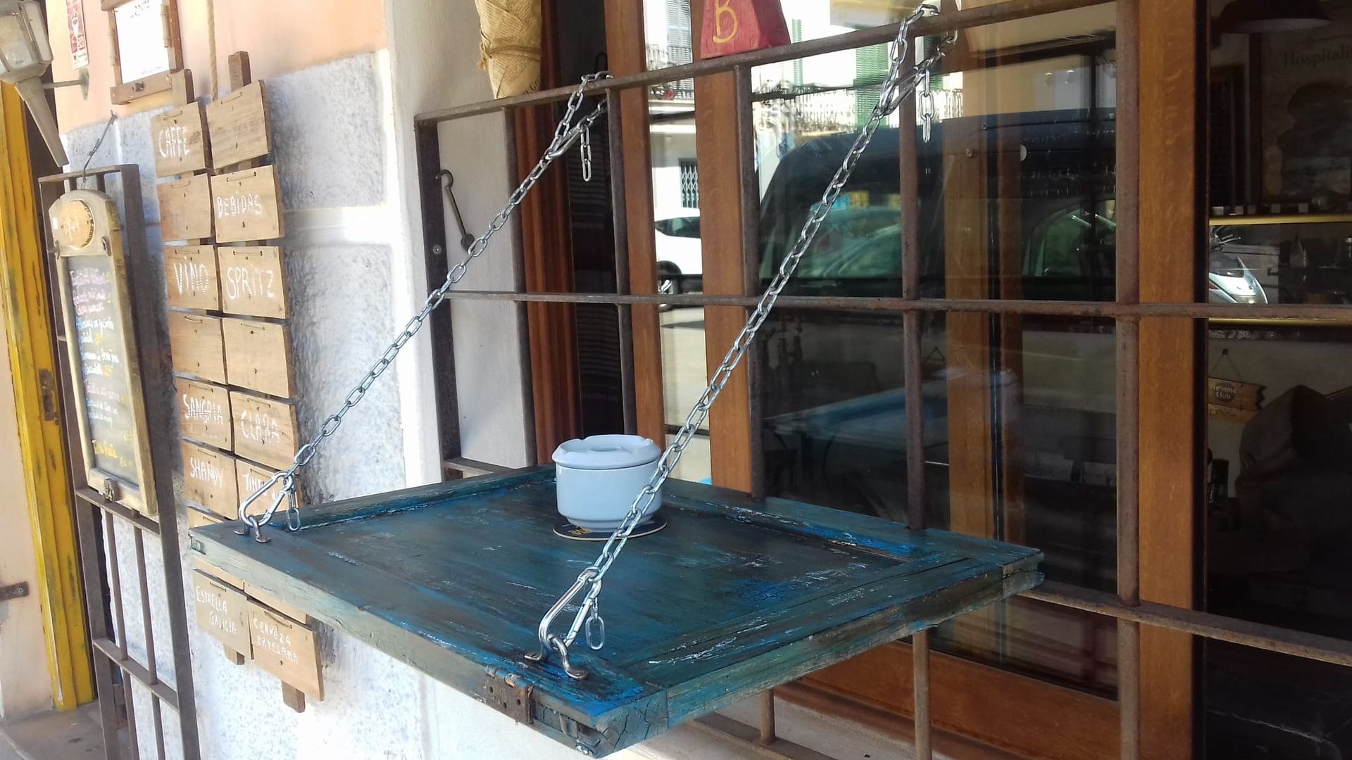 Una mesa azul con un cuenco encima cuelga de cadenas en el exterior de un edificio.