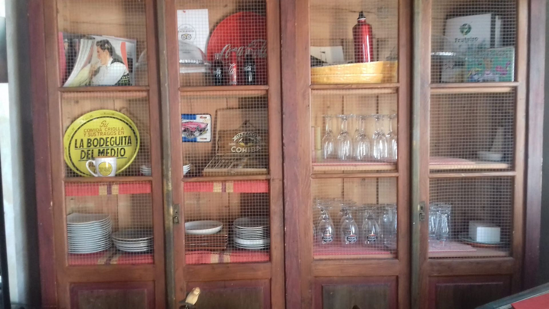 Un armario de madera con puertas de cristal y estantes llenos de platos y vasos.