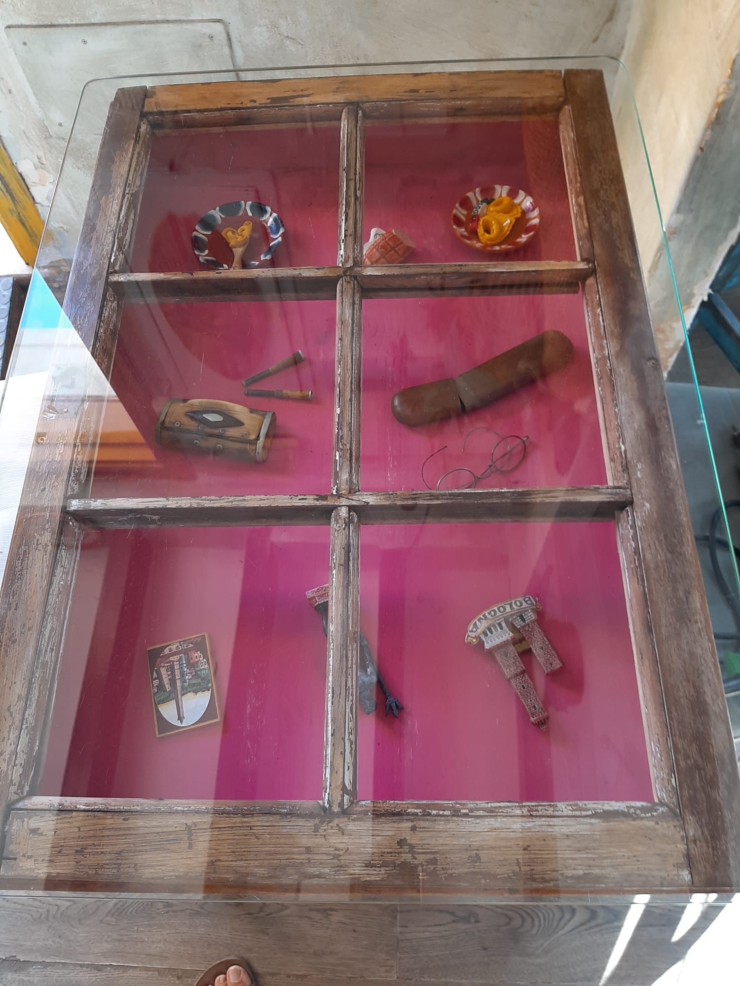 Una mesa de madera con tapa de cristal y una vitrina llena de diversos artículos.