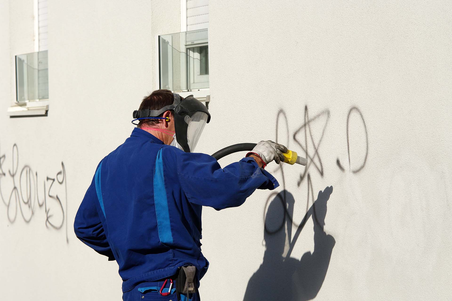 Un homme en tenue de travail enlevant un graffiti sur le mur
