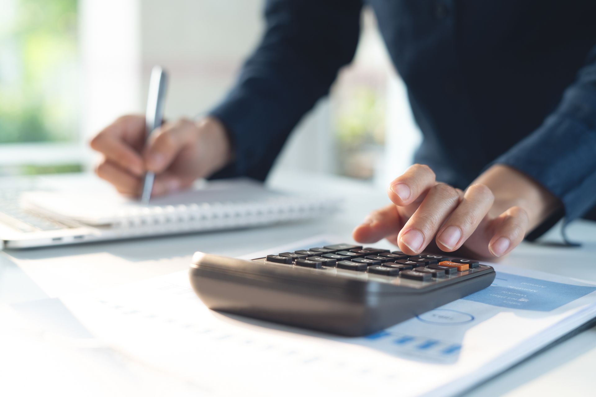 Une personne utilise une calculatrice et prend des notes manuelles sur un calepin.