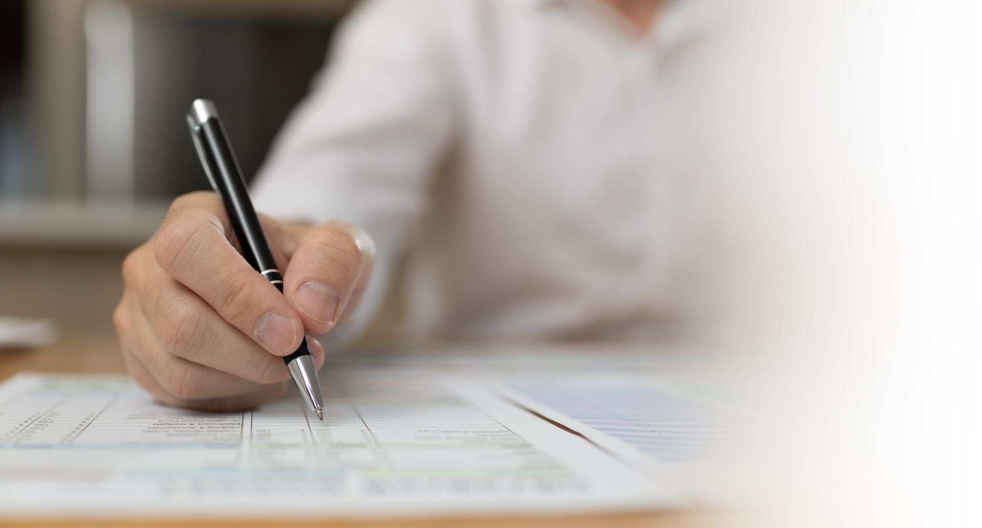 Gros plan d'une main écrivant au stylo noir sur un document posé.