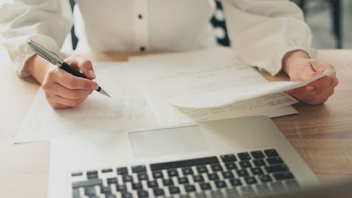 Une personne devant des papiers et un ordinateur portable.