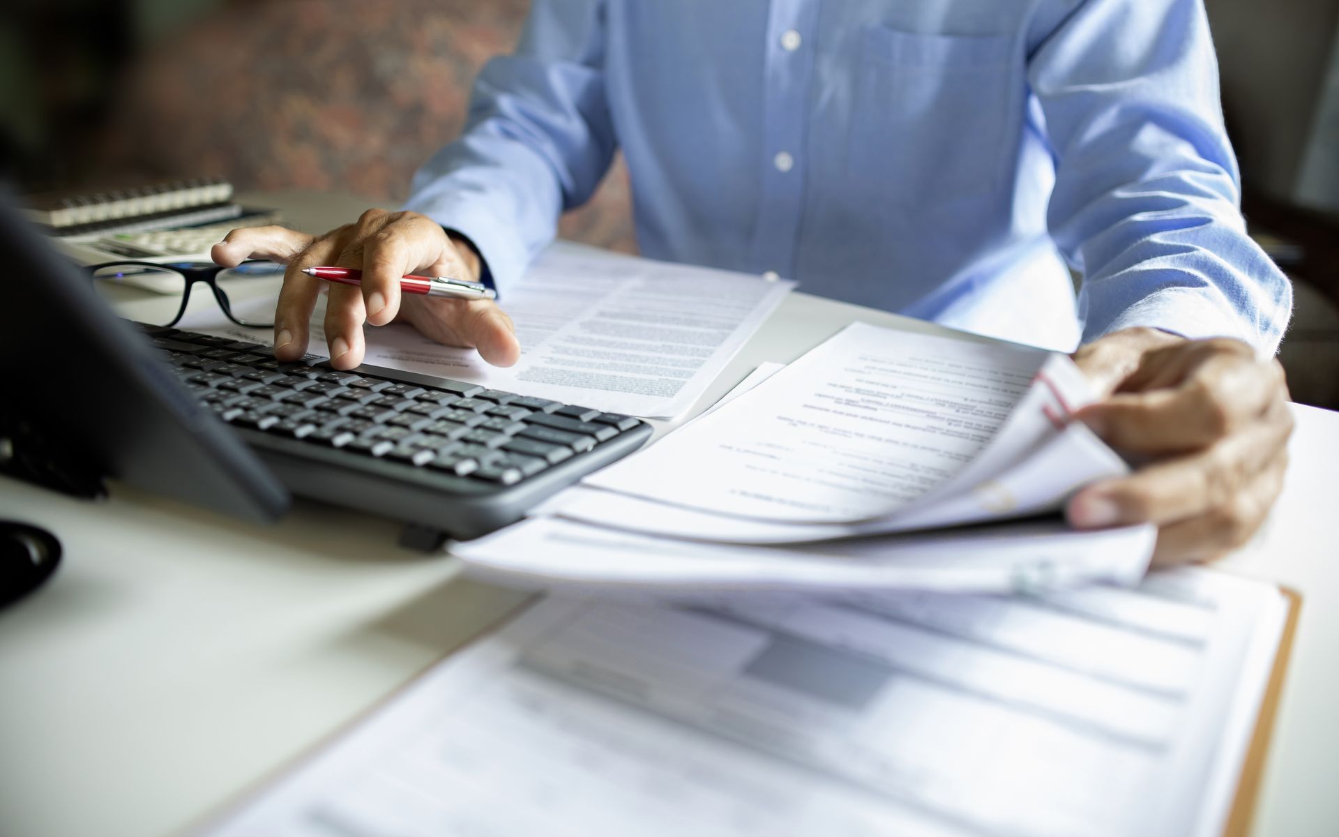 Une personne relit des documents à côté d'un ordinateur portable posé sur un bureau.