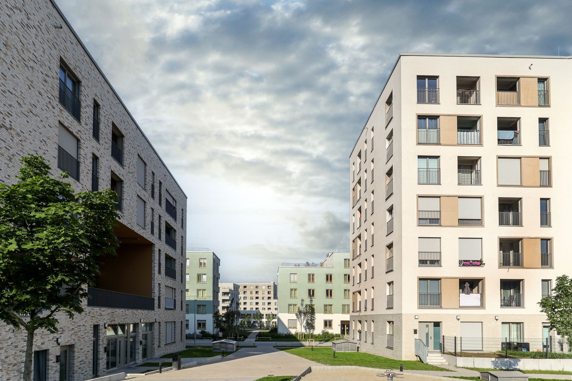 Des immeubles d'appartements modernes bordent une cour intérieure tranquille sous un ciel nuageux.