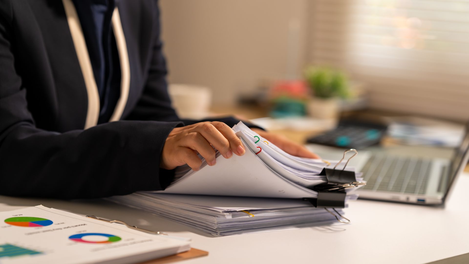 Une personne feuillette un rapport à côté d'un ordinateur portable, avec des graphiques et des documents sur un bureau.