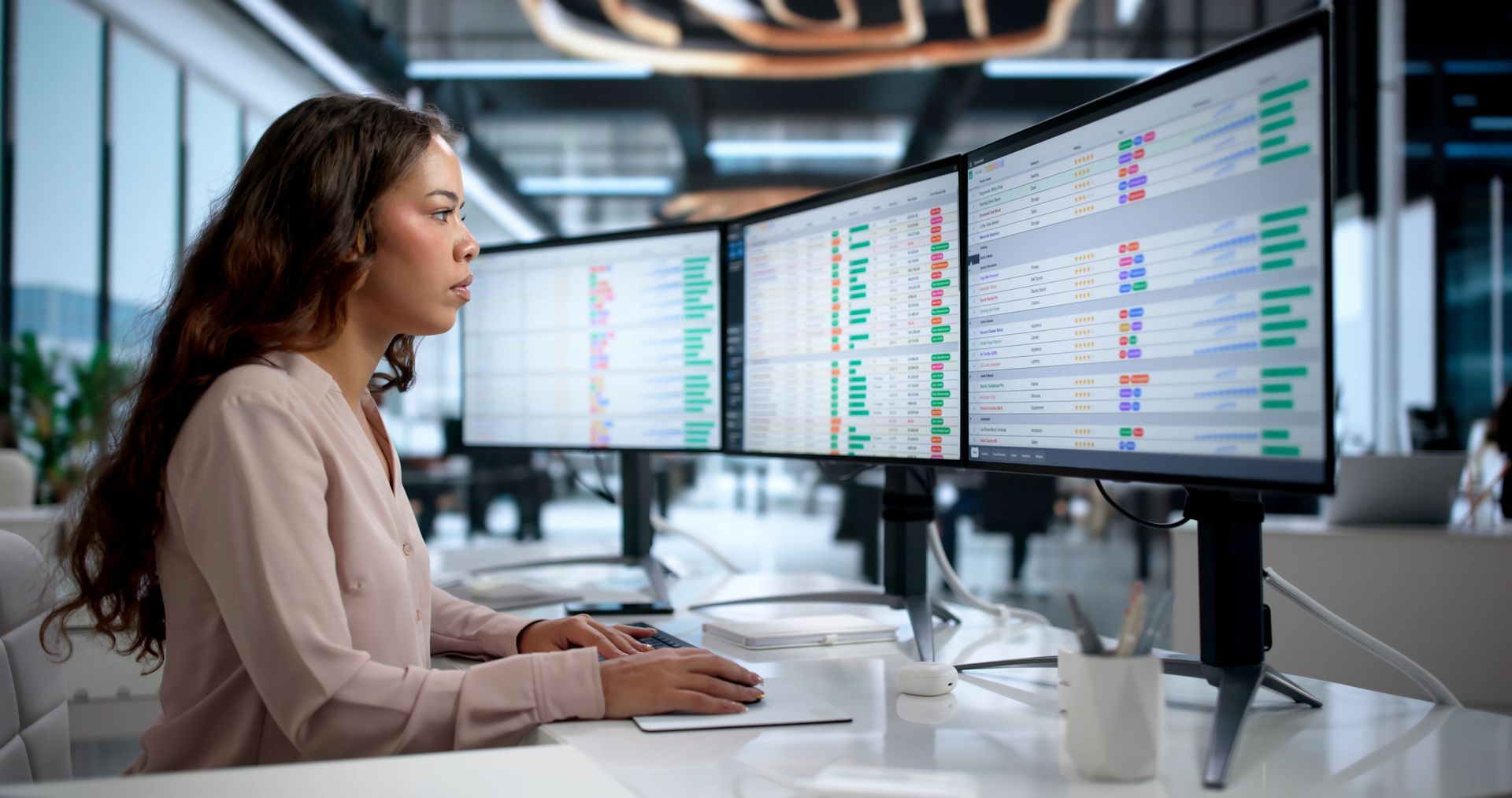 Femme travaillant à un bureau avec plusieurs grands écrans affichant des données boursières dans un bureau moderne.