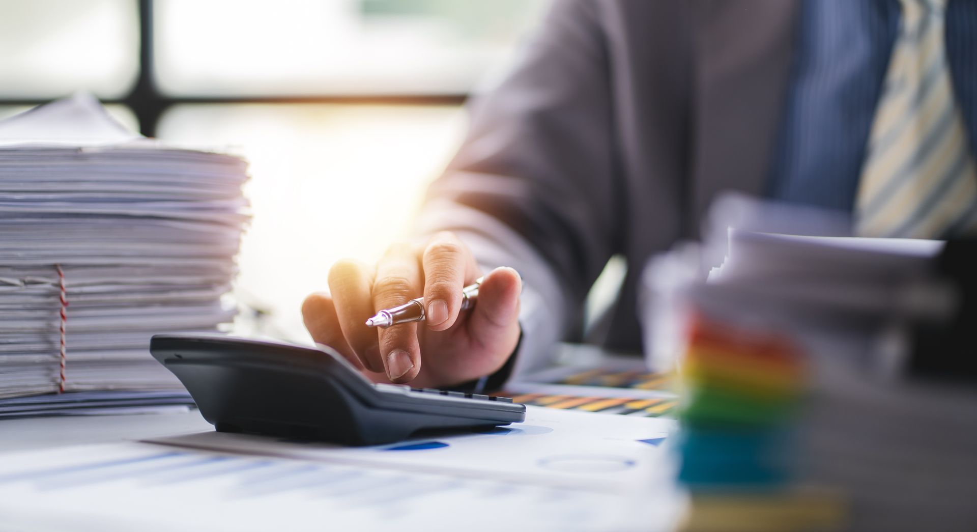 Une personne utilise une calculatrice à un bureau entouré de piles de papiers.