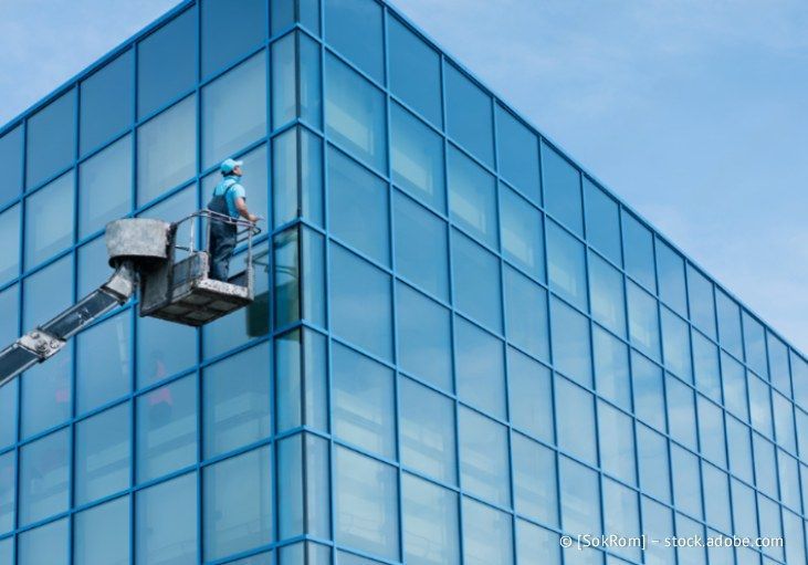 Fensterputzer reinigt in einem Aufzug die Ecke eines blauen Glasgebäudes.