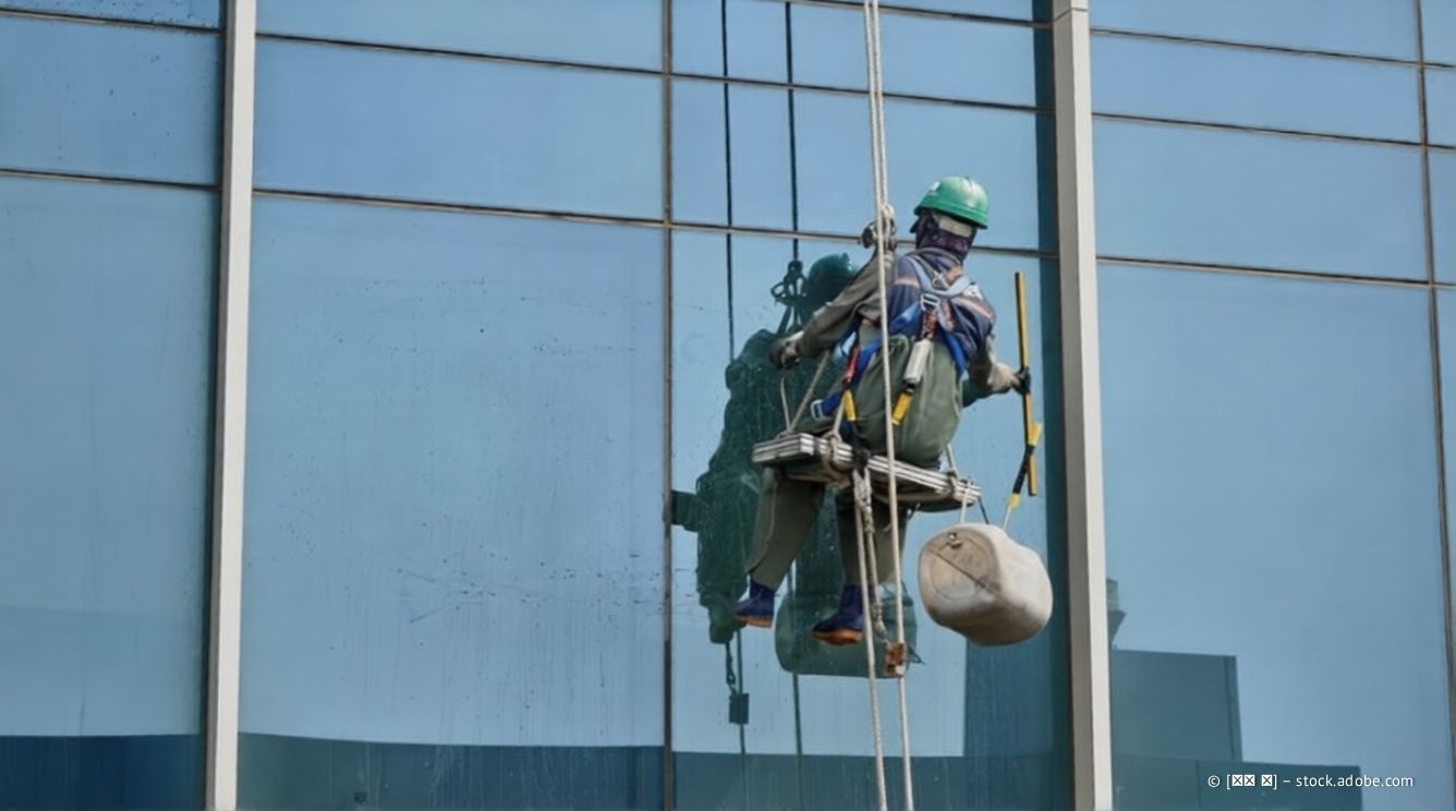 Ein Fensterputzer, der an Seilen hängt, reinigt die Glasfenster eines hohen Gebäudes.