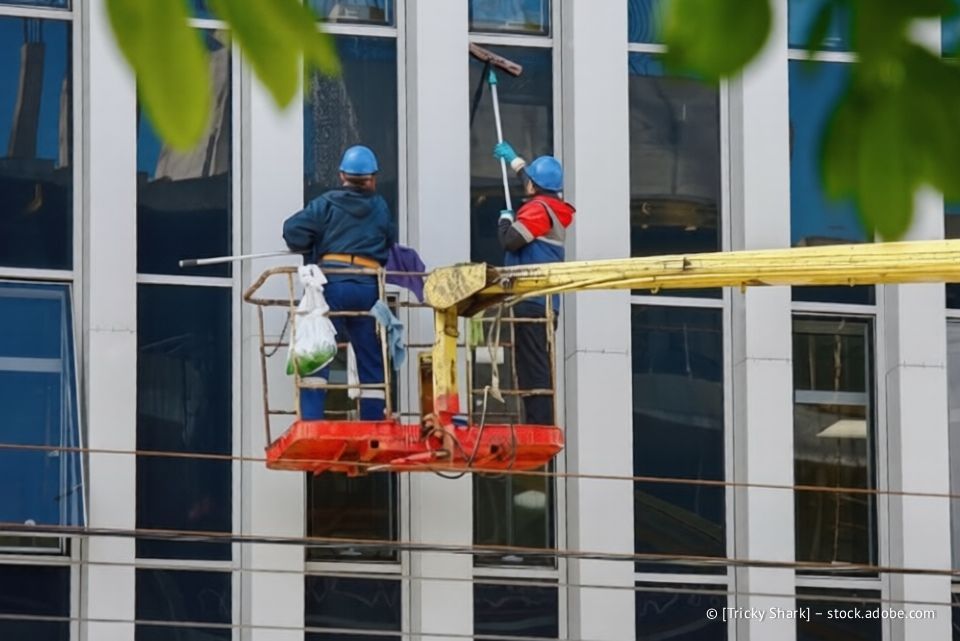 Zwei Fensterputzer reinigen in einem Aufzug die Fenster eines Wolkenkratzers.