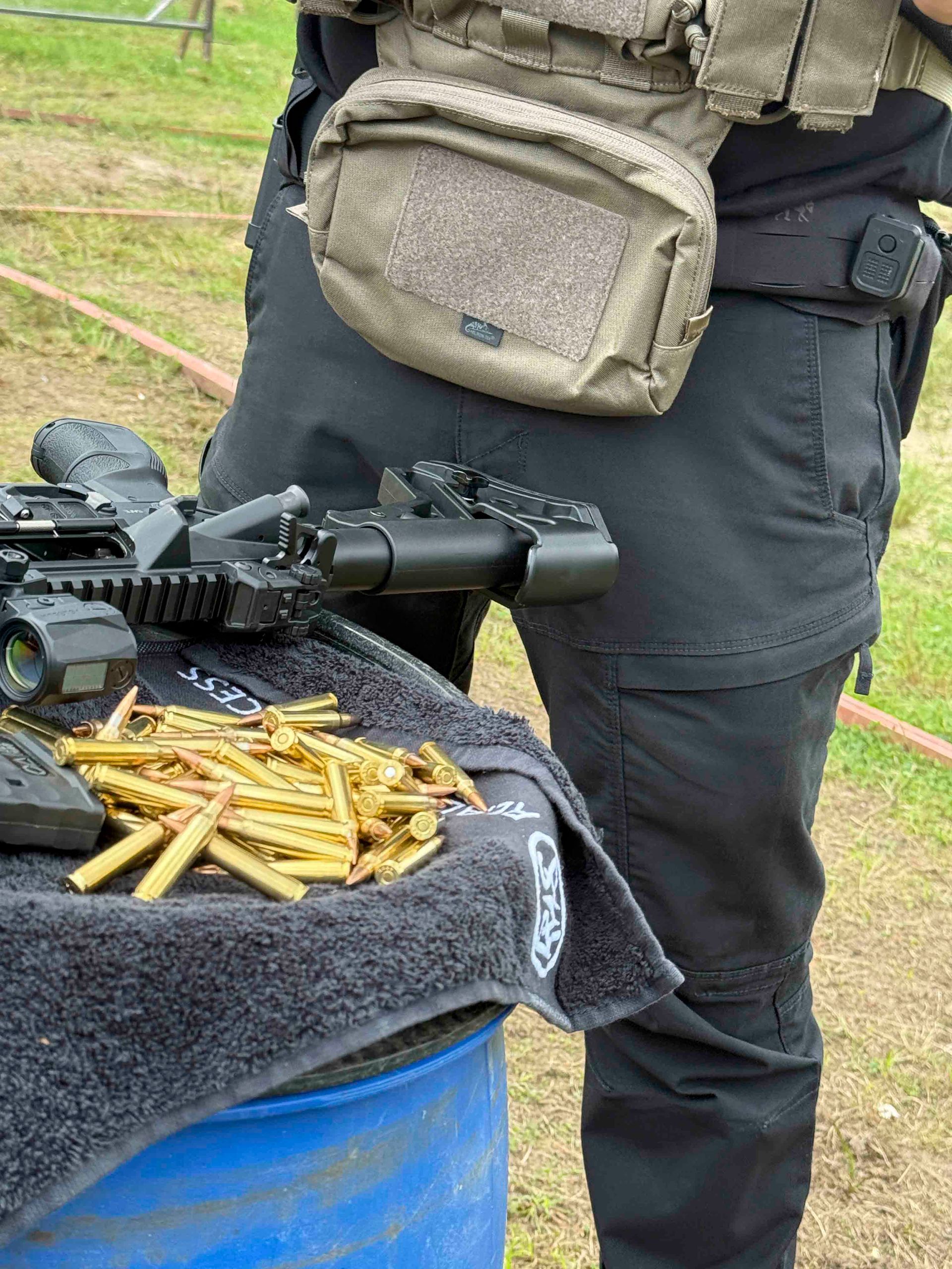 Eine Person in taktischer Ausrüstung auf einem Schießstand, mit einer Handfeuerwaffe, Munition und einer Brusttasche.
