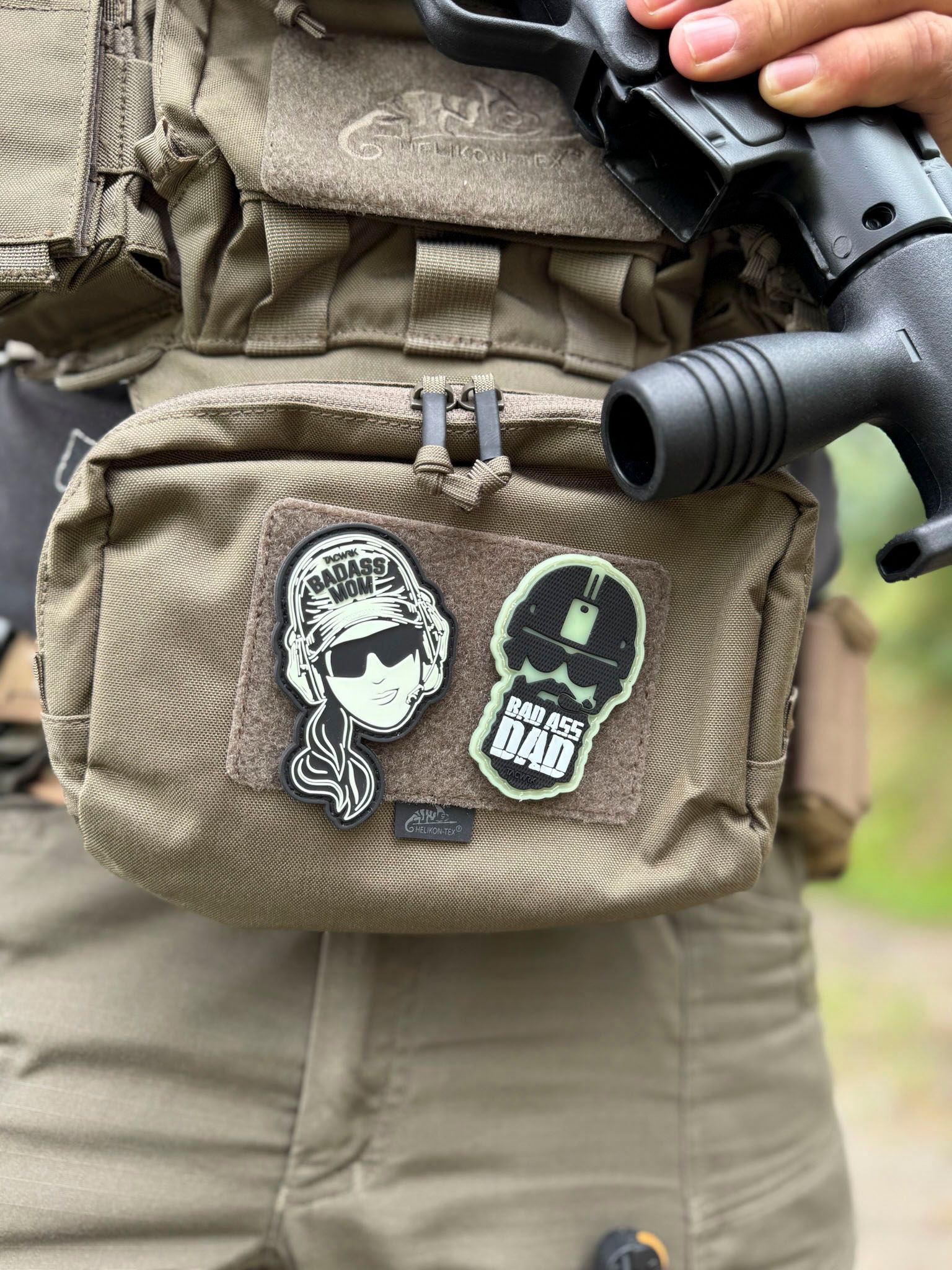 Eine Person in taktischer Ausrüstung mit Aufnähern an einer Tasche. Sie hält eine Schusswaffe.