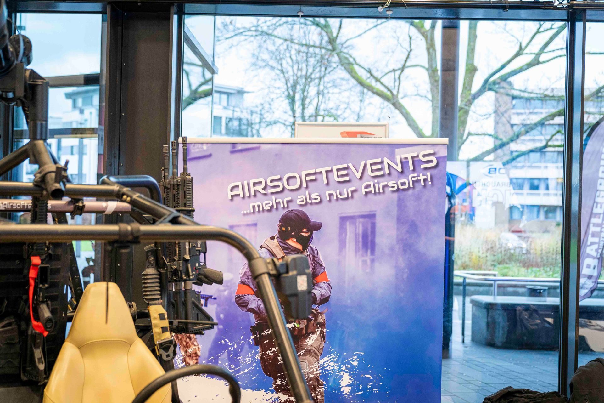 Banner für Airsoft-Veranstaltungen. Eine Person in Ausrüstung, mit Spritzeffekten. Gebäude im Hintergrund.
