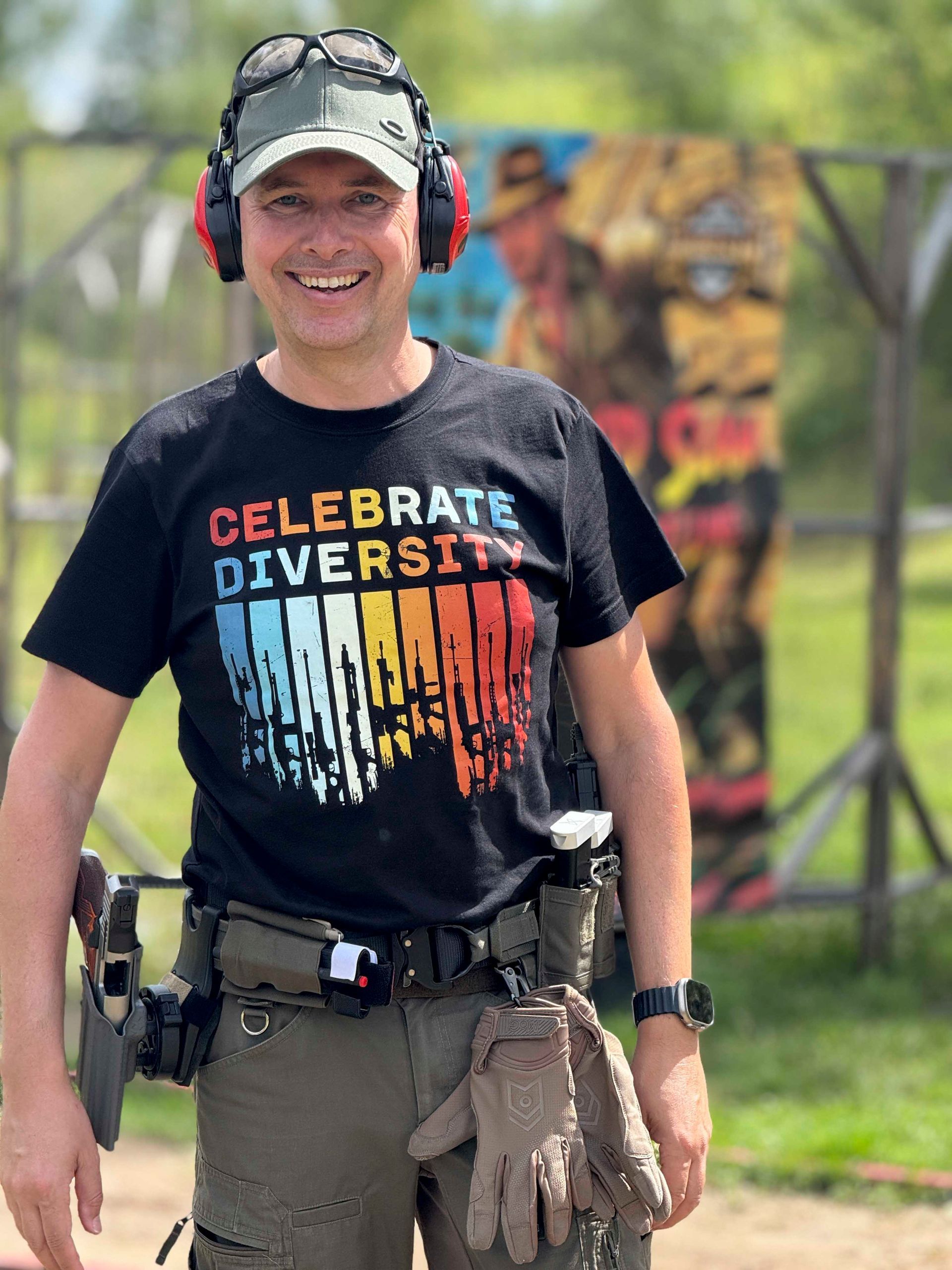 Mann im T-Shirt mit der Aufschrift „Celebrate Diversity“, mit Gehörschutz, auf einem Schießstand im Freien.