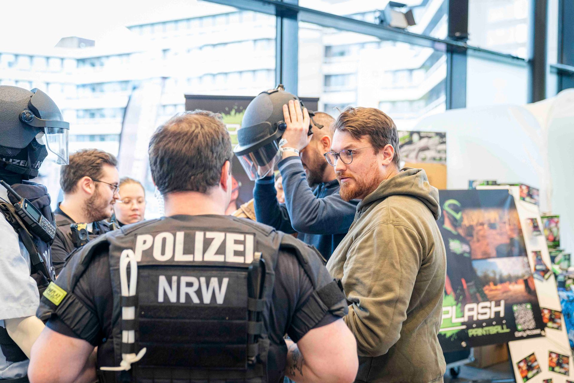 Ein Polizist in Schutzweste setzt einem Mann einen Helm auf. Andere beobachten das Geschehen.