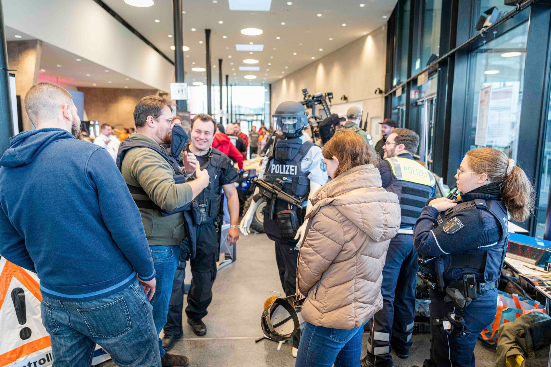 Menschen interagieren in einem öffentlichen Raum mit einem schwer gepanzerten Polizisten.