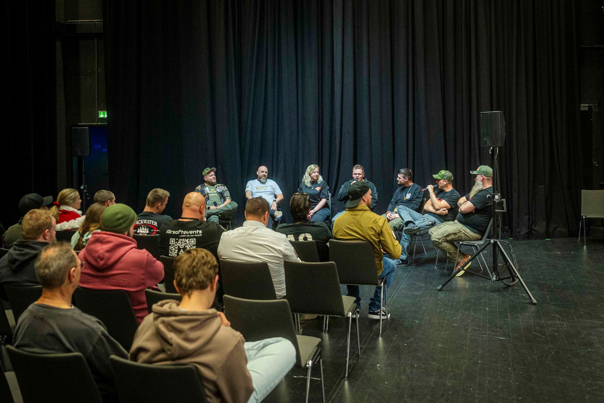 Podiumsdiskussion auf der Bühne mit Publikum vor den Zuhörern, schwarzer Hintergrund.
