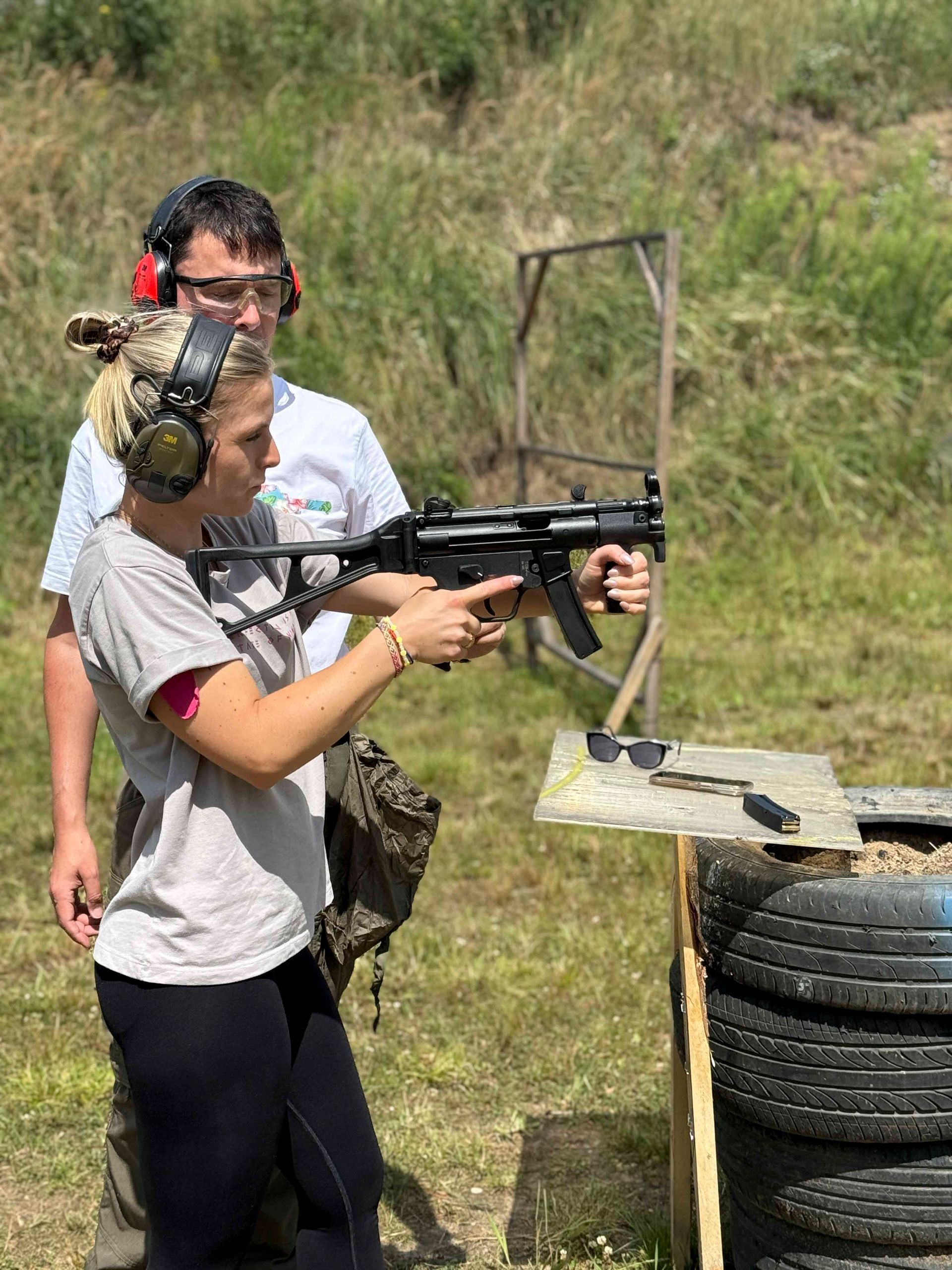 Eine Frau schießt mit einer Schusswaffe auf einem Schießstand, ein Ausbilder schaut zu.