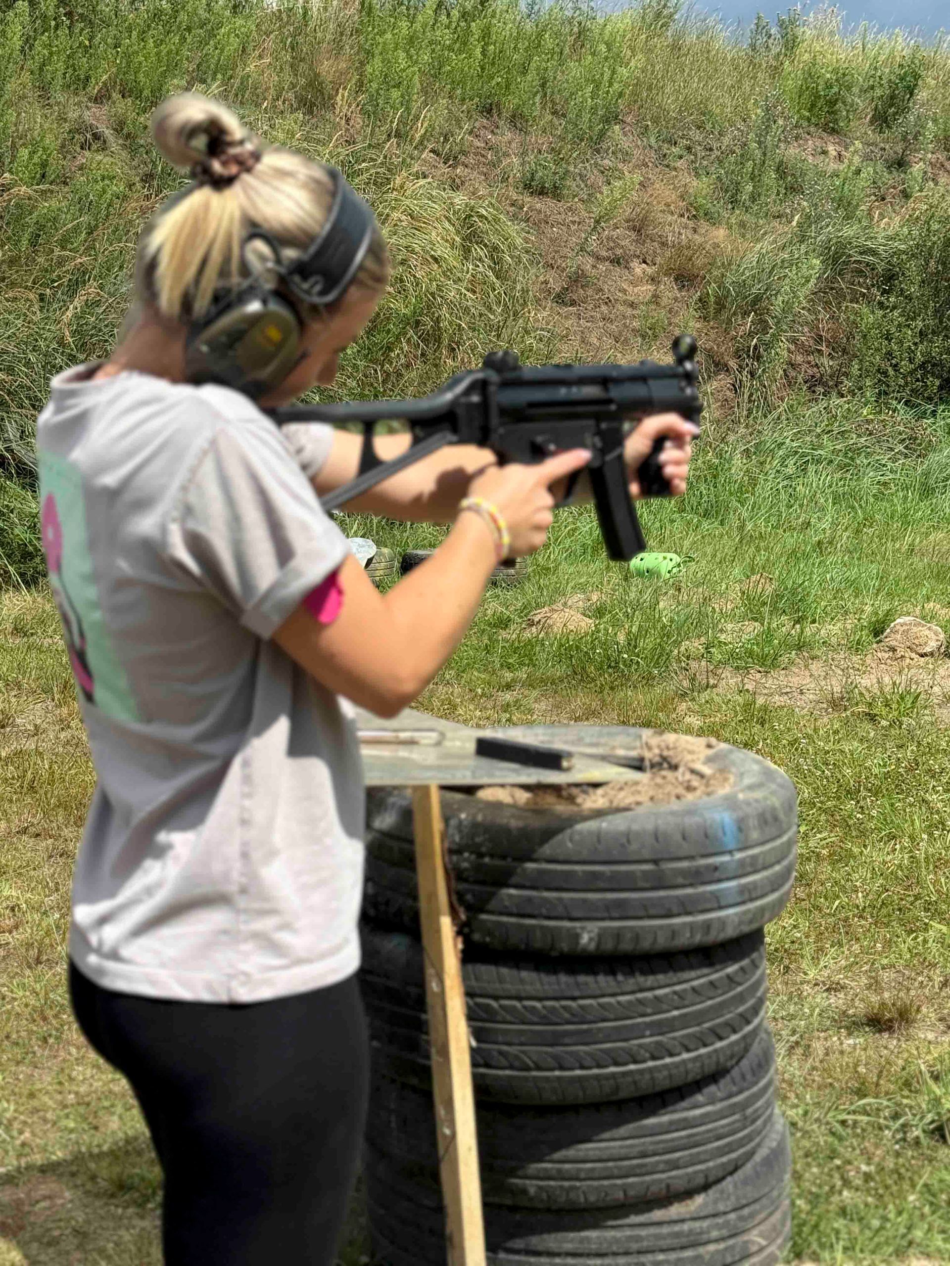 Eine Frau feuert mit Gehörschutz auf einem Schießstand im Freien in der Nähe von Reifen mit einer Maschinenpistole.
