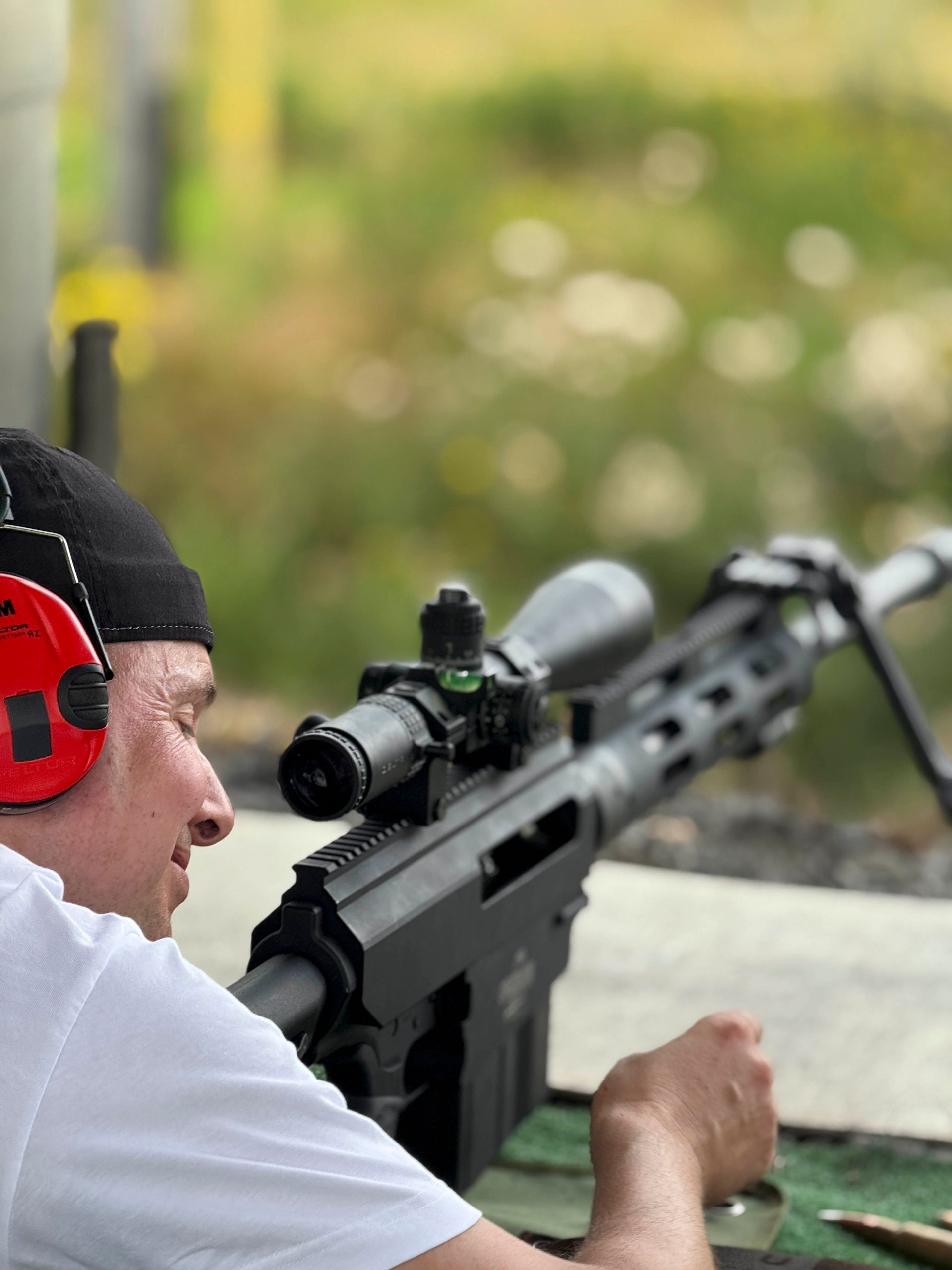 Eine Person, die auf einem Schießstand im Freien mit einem Gewehr mit Zielfernrohr zielt, trägt Gehörschutz