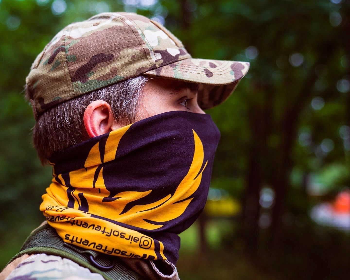 Eine Person mit Tarnmütze und Gesichtsmaske mit gelbem Flammenmuster steht im Freien.