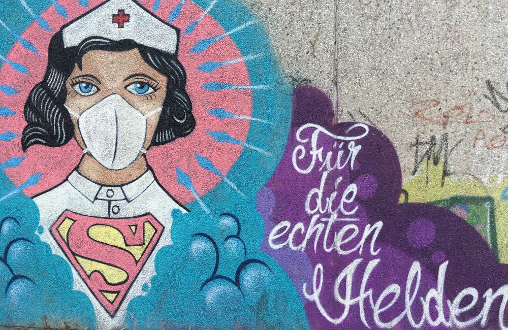 Graffiti einer Krankenschwester mit Maske und Superman-Symbol, dazu deutscher Text: „Für die wahren Helden“.