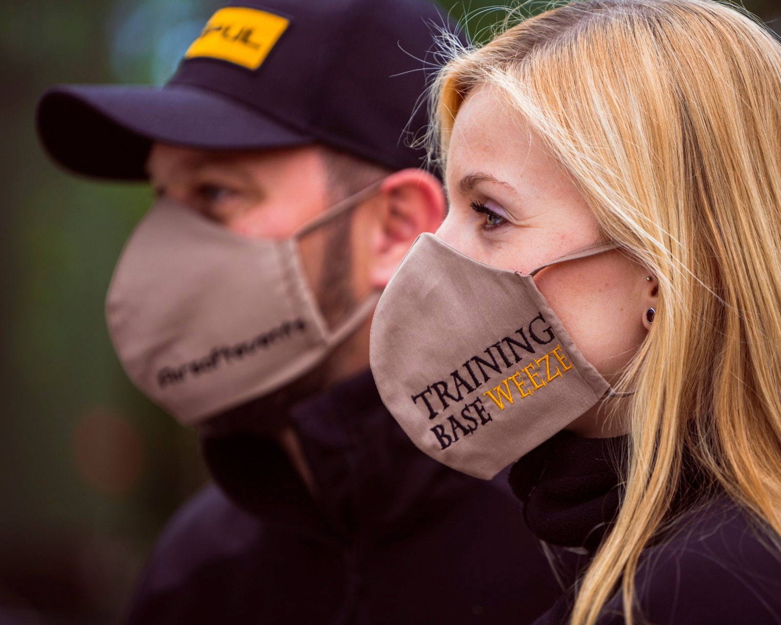 Zwei Personen tragen beige Gesichtsmasken mit der Aufschrift 