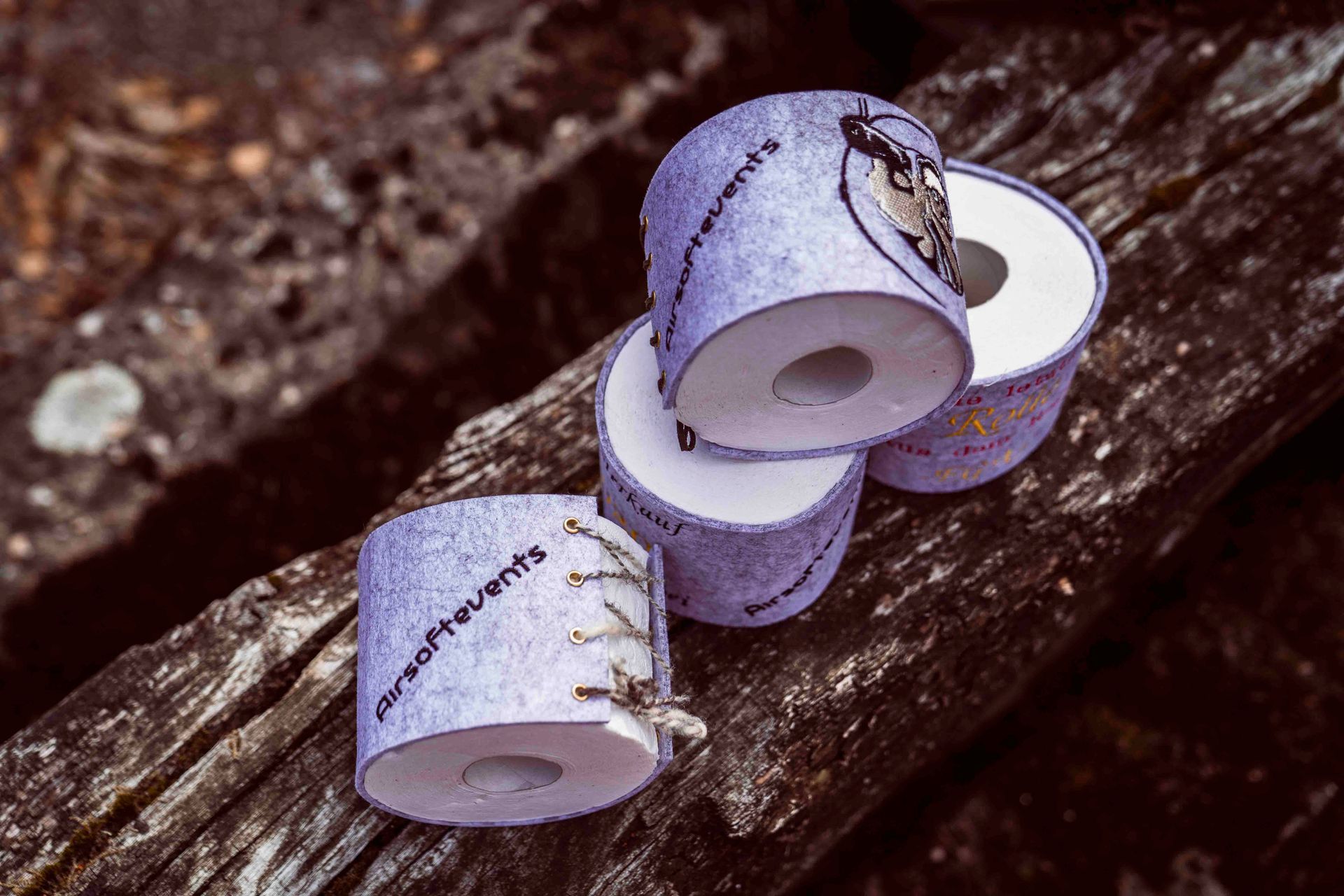 Vier lila Toilettenpapierrollen mit Text und einem Hundebild sind auf verwittertem Holz gestapelt.