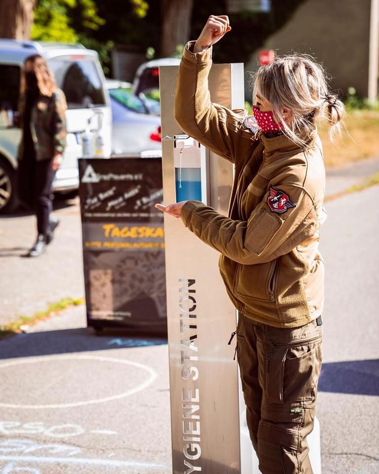 Eine Frau benutzt Händedesinfektionsmittel an einer „Hygienestation“ im Freien. Sie trägt eine Gesichtsmaske