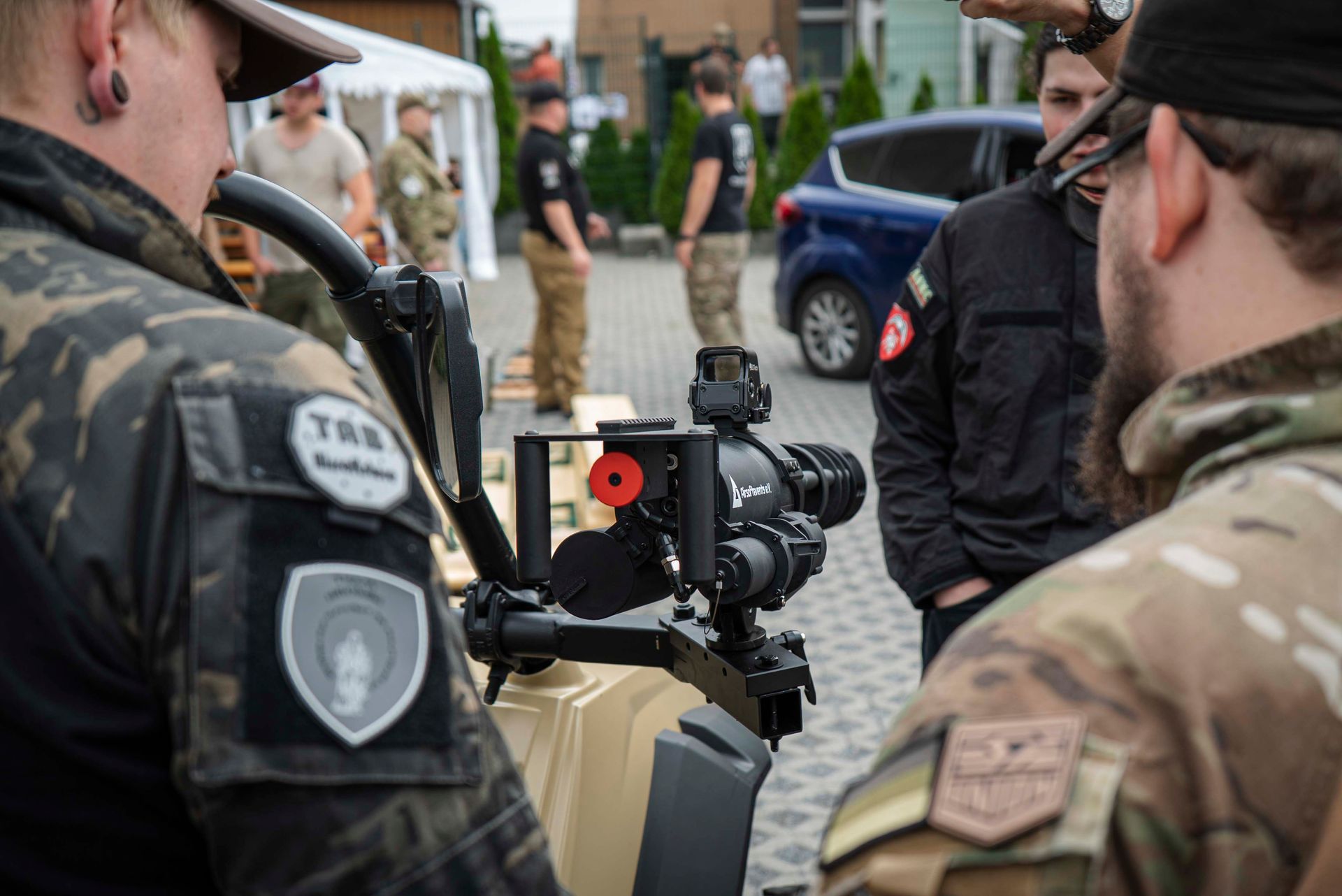 Menschen untersuchen im Freien ein Gerät mit Kamera. Soldaten in Tarnkleidung. Einige schauen in die Kamera