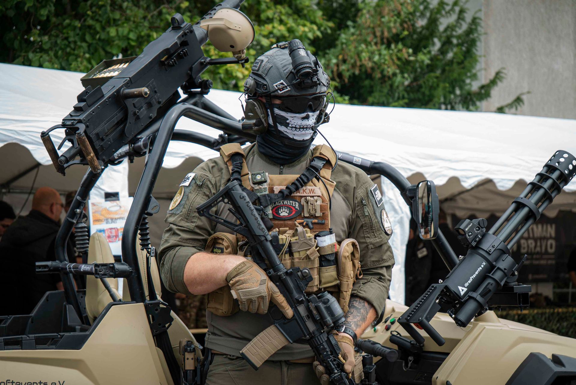 Ein Soldat in taktischer Ausrüstung mit Totenkopfmaske steht neben einem Fahrzeug mit montierten Maschinengewehren.