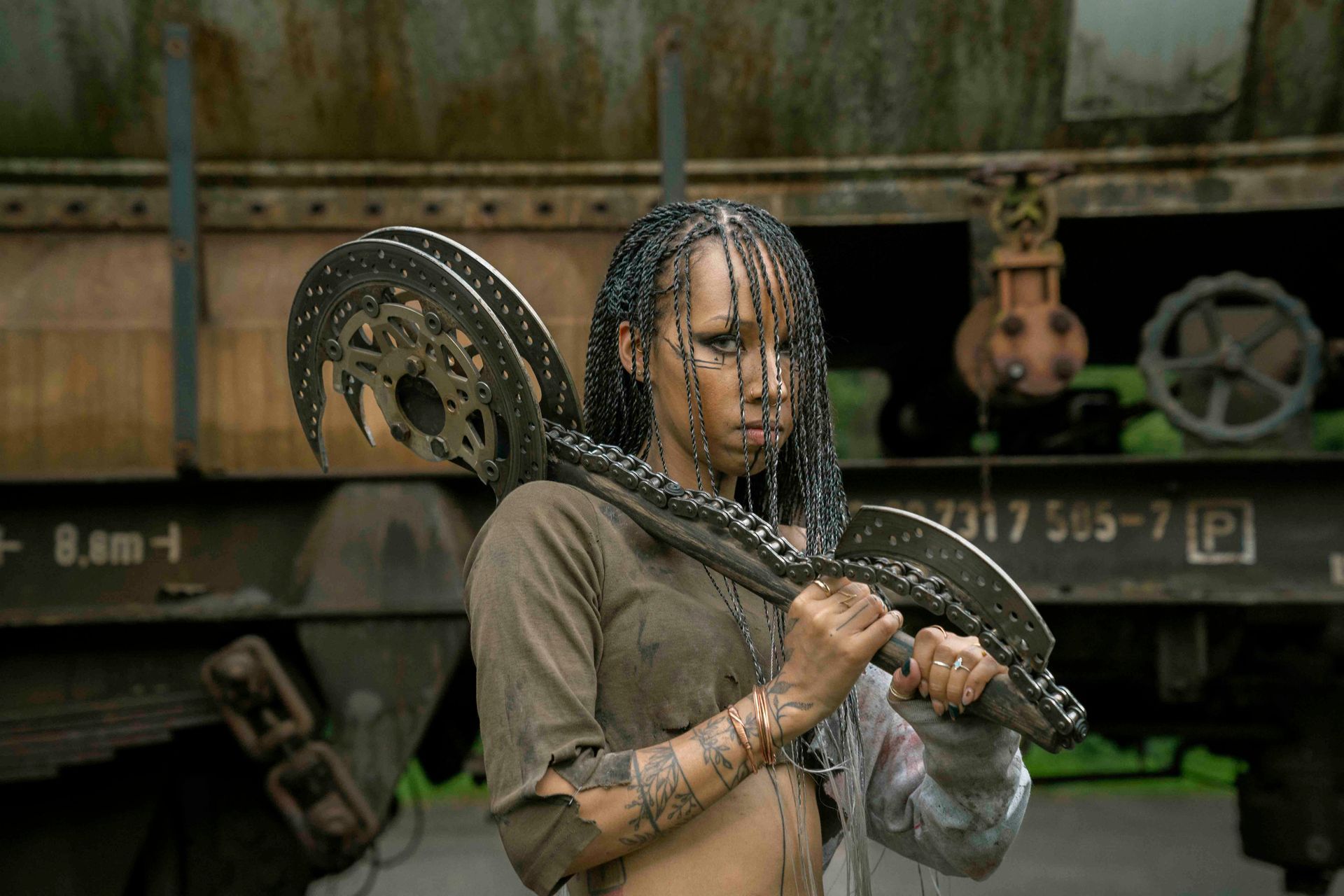 Frau hält eine große Waffe mit Zahnrädern und steht vor einem Eisenbahnwaggon.