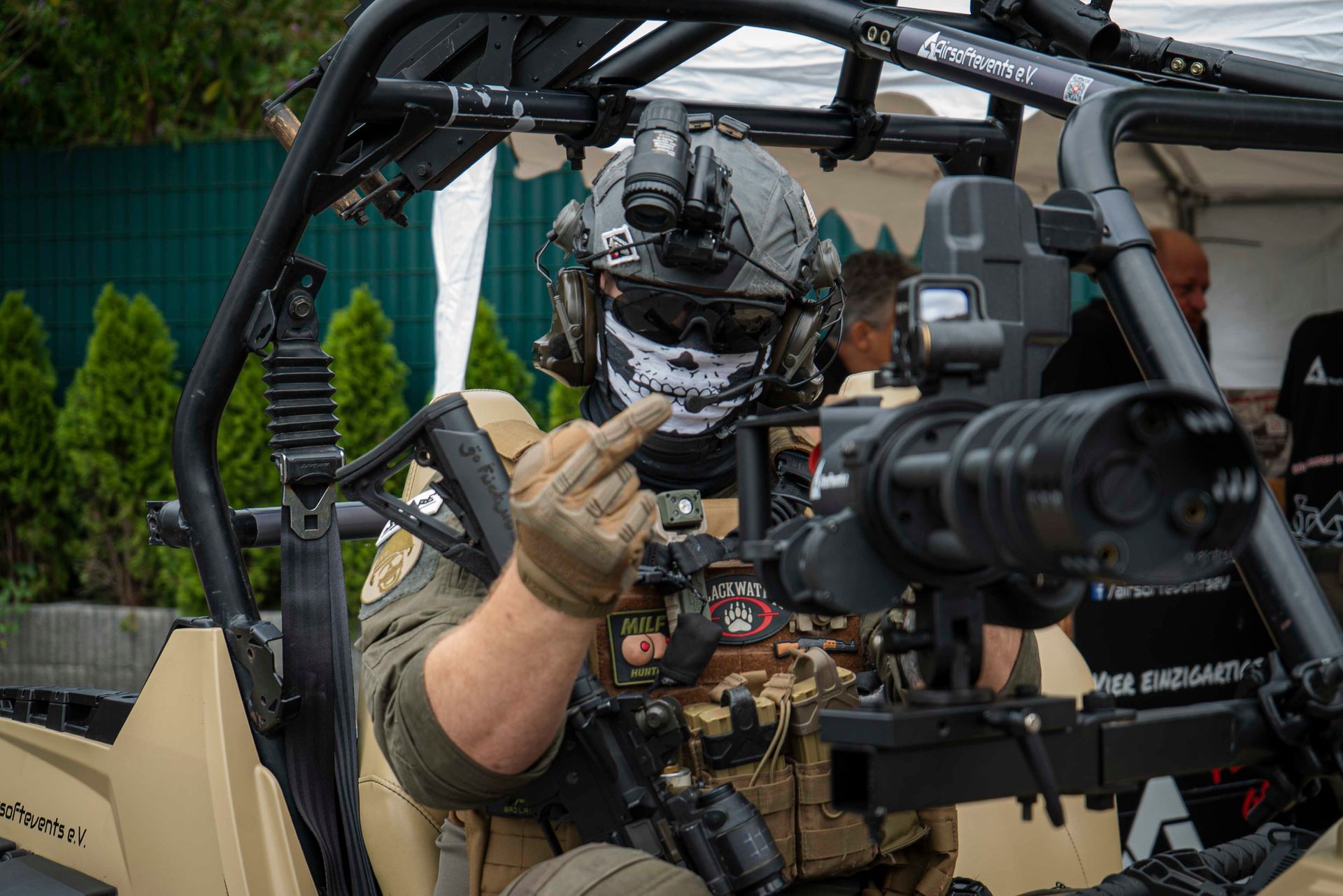 Eine Person in taktischer Ausrüstung, Maske und Helm zeigt den Mittelfinger, während sie sich in einem Fahrzeug befindet.