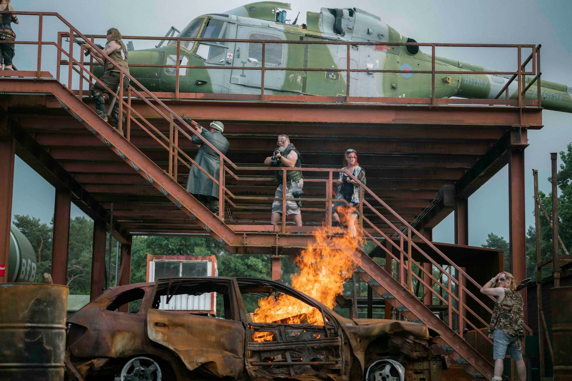 Menschen auf einer Plattform neben einem Hubschrauber beobachten ein brennendes Auto. Flammen umhüllen das Fahrzeug