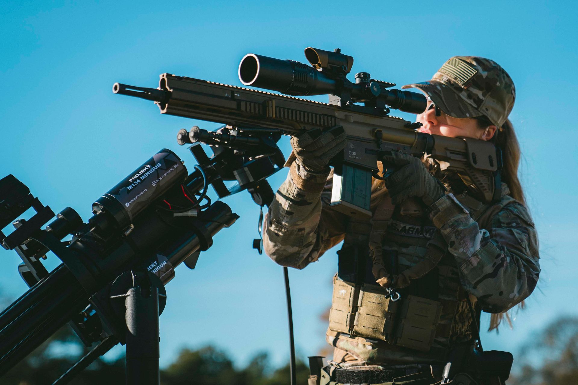 Frau zielt im Freien mit einem Gewehr mit Zielfernrohr, trägt Tarnkleidung.