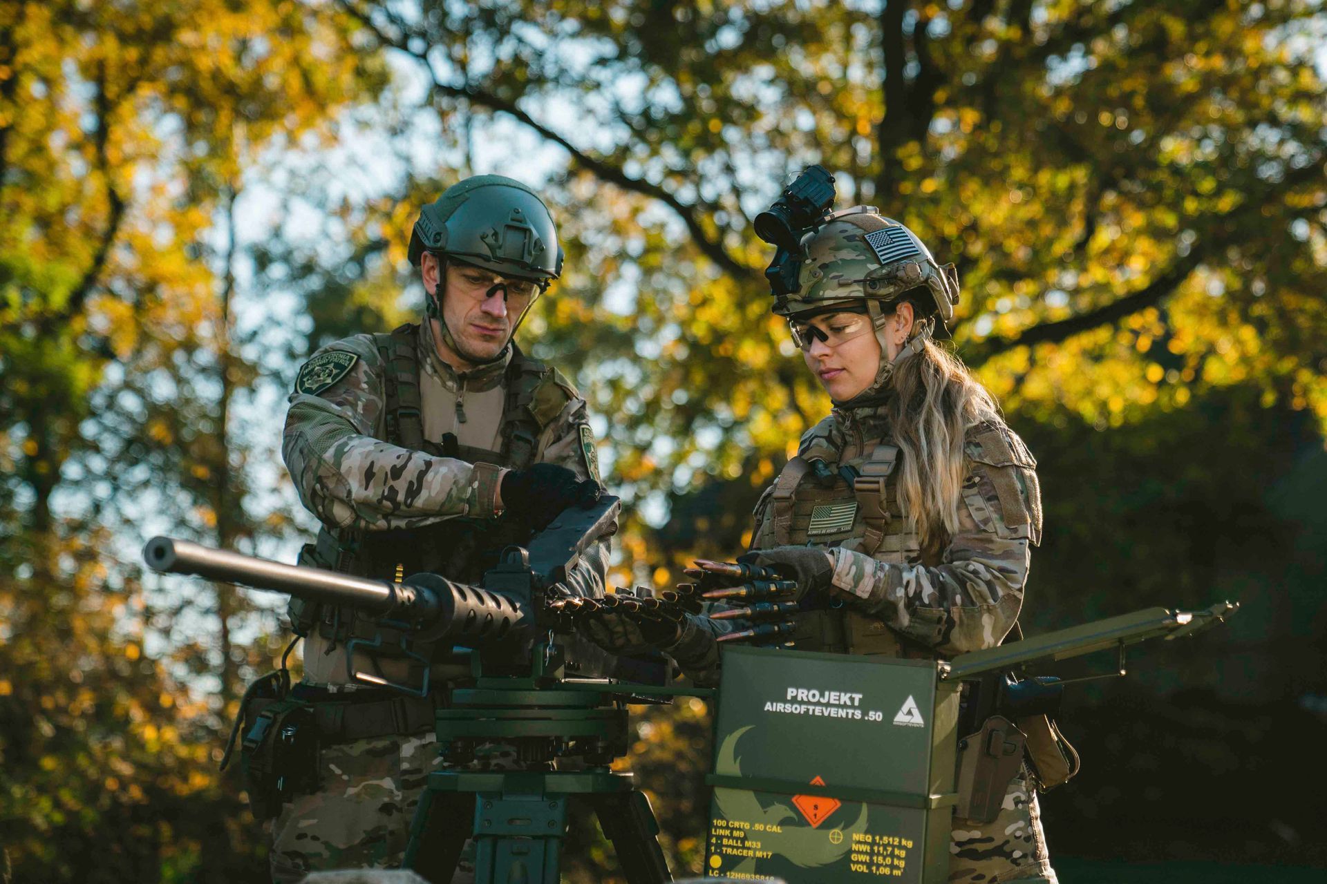 Zwei Soldaten untersuchen im Freien ein montiertes Maschinengewehr. Einer trägt einen Helm mit Nachtsichtgerät.