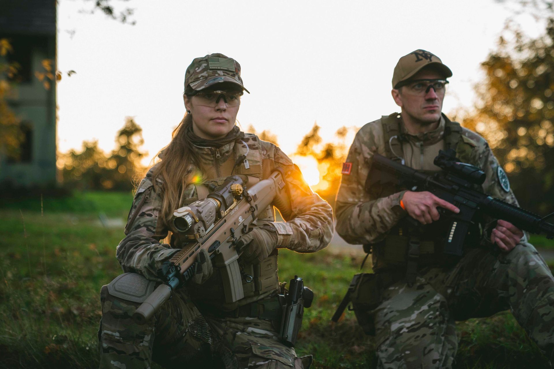 Zwei in Tarnkleidung gekleidete Personen mit Gewehren, die wachsam wirken. Im Freien, kurz vor Sonnenuntergang.