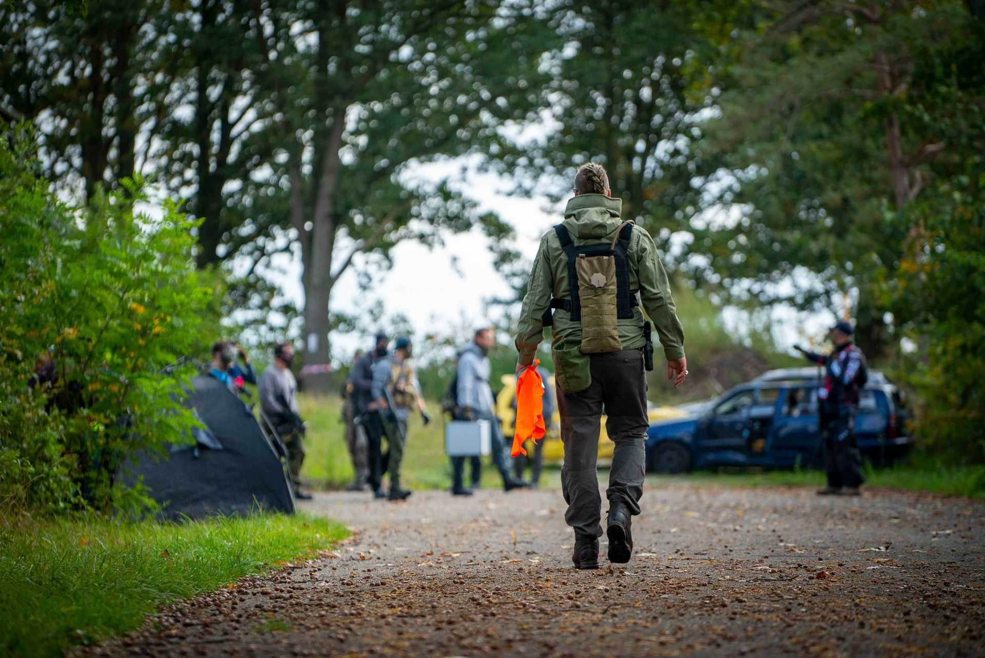 Ein Mann mit Rucksack geht einen Feldweg entlang auf eine Gruppe von Menschen zu