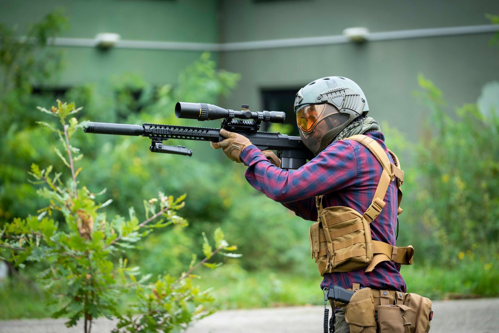 Eine Person, die in freier Natur mit einem Gewehr mit Zielfernrohr zielt und dabei einen Helm und taktische Ausrüstung trägt.
