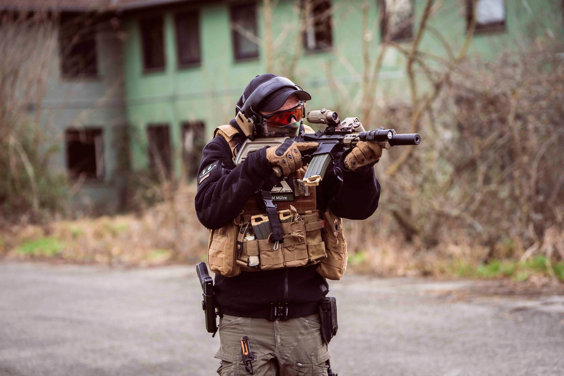 Eine Person in taktischer Ausrüstung zielt mit einem Gewehr vor einem verwitterten Gebäude.