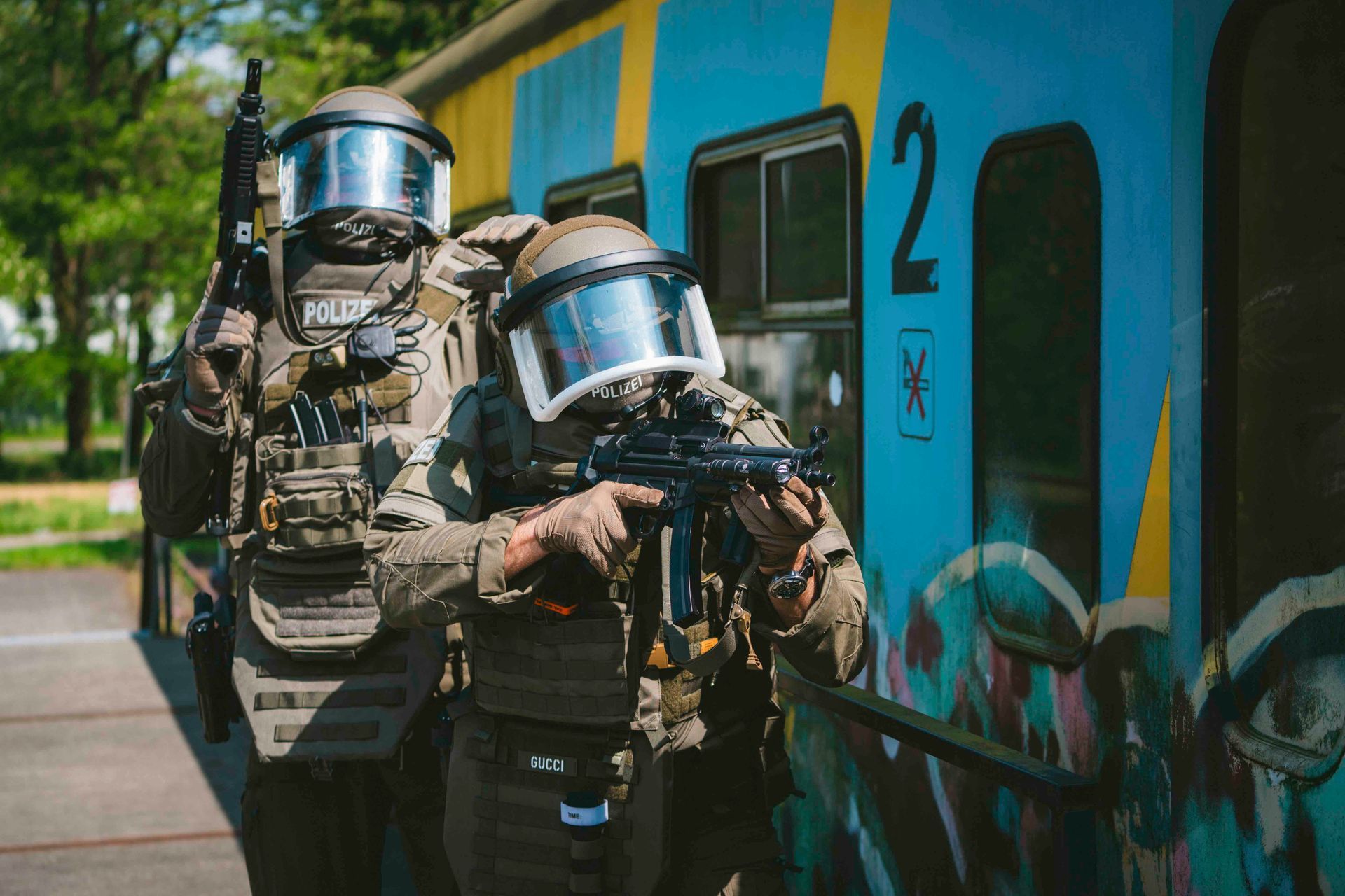 Zwei bewaffnete, gepanzerte Polizisten in der Nähe eines mit Graffiti besprühten Eisenbahnwaggons.