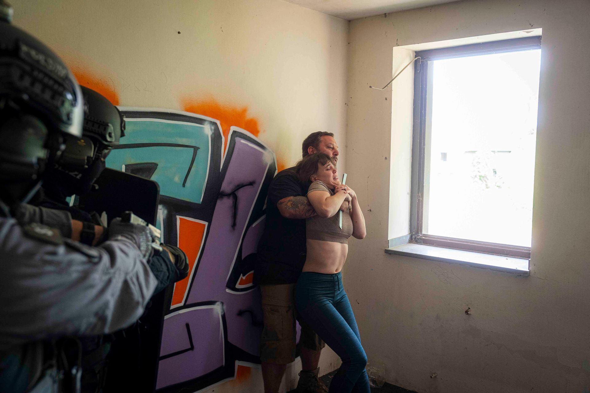 Ein SWAT-Team zielt auf einen Mann, der eine Frau in einem mit Graffiti besprühten Raum festhält.