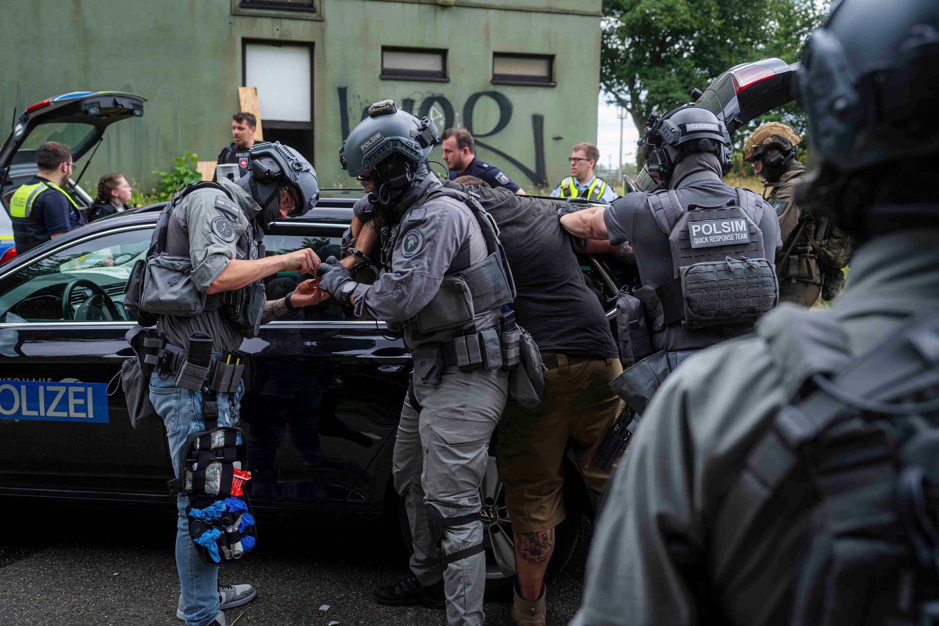 Polizisten halten eine Person neben einem schwarzen Polizeiwagen fest.