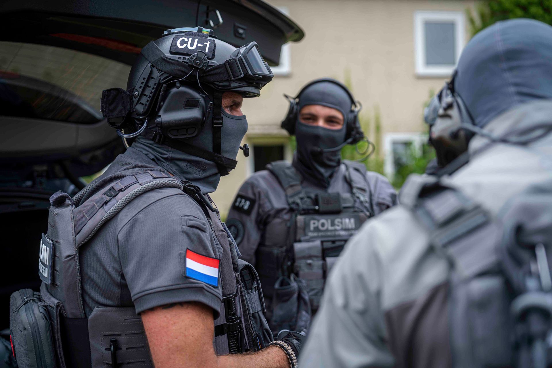 Drei taktische Polizisten in dunklen Uniformen, einer davon mit einem Aufnäher der niederländischen Flagge