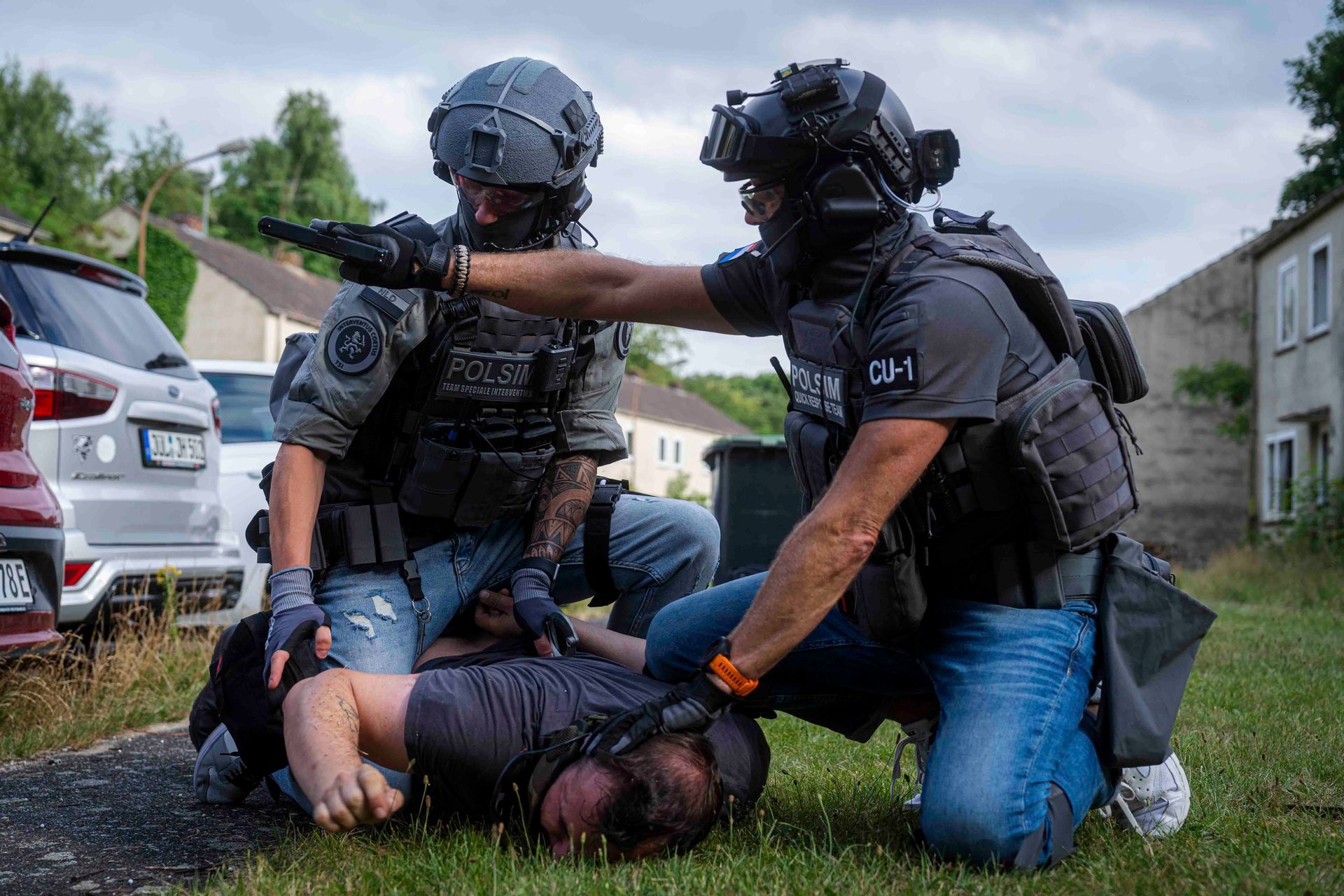 Zwei bewaffnete Polizisten halten eine Person im Freien am Boden fest.