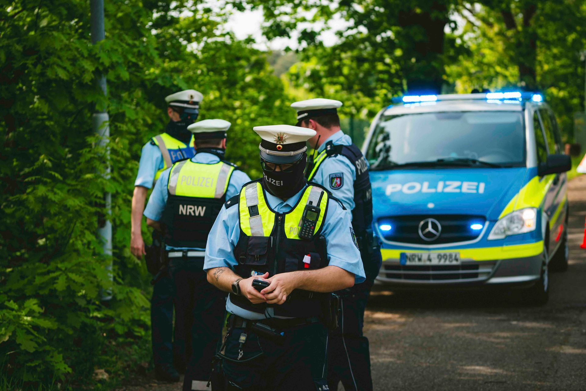Polizisten in Westen und Mützen stehen im Freien neben einem blau-gelben POLIZEI-Van.