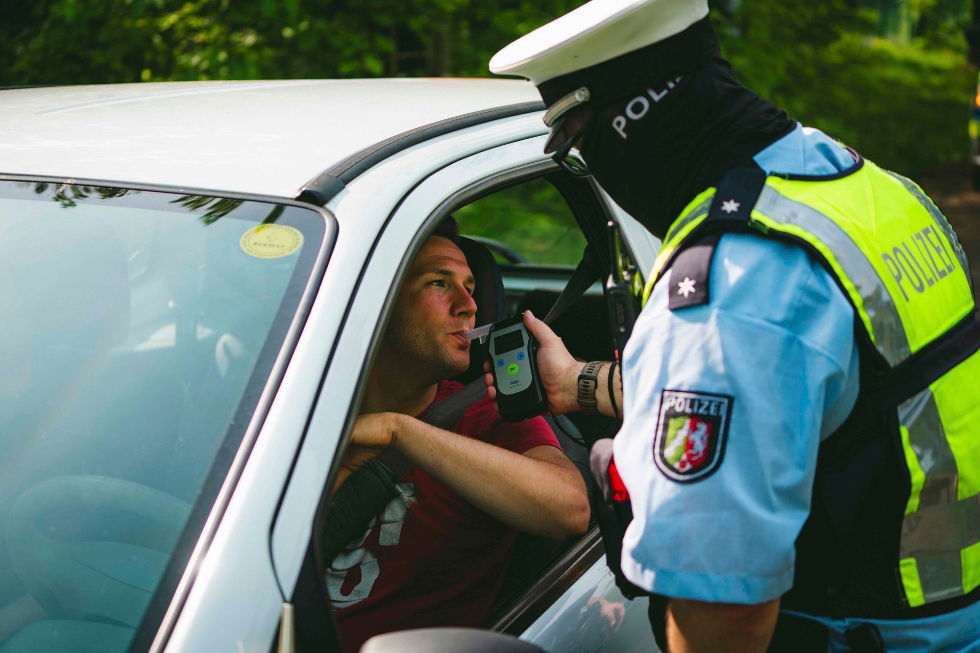 Ein Polizist führt bei einem Fahrer in einem weißen Auto einen Atemalkoholtest durch.